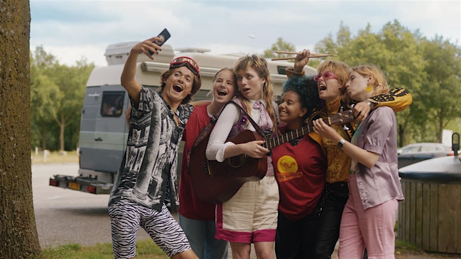 photo from the movie OKTHANKSBYE showing six (6) teens taking a selfie. One of them holds a guitar, another is holding a pair of drumsticks.